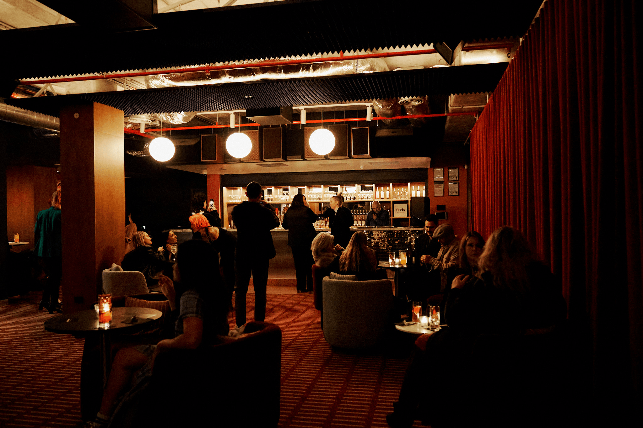 The inside of a bar with people drinking and a lit up standing area.